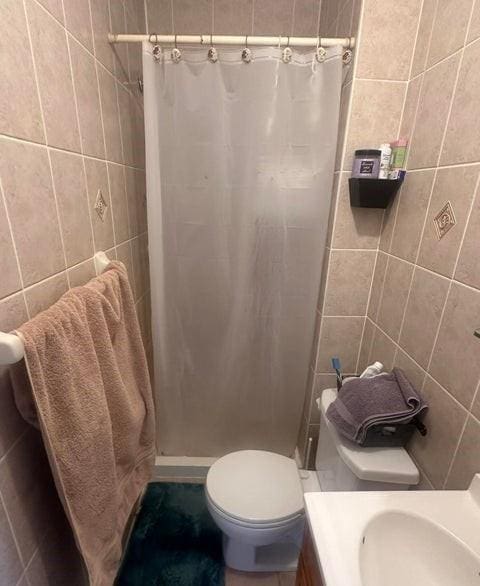 bathroom with a shower stall, toilet, and tile walls