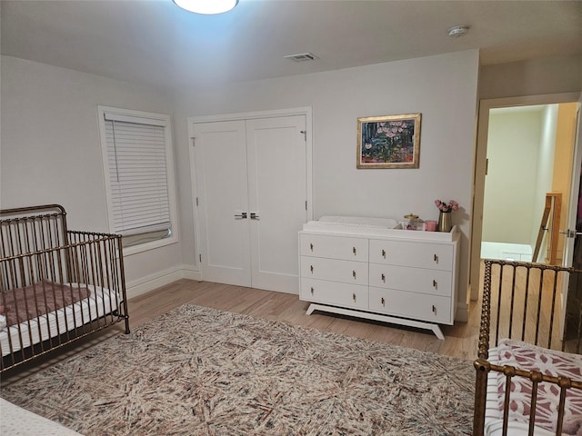 bedroom with a nursery area, light hardwood / wood-style floors, and a closet