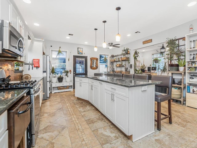 kitchen with white cabinetry, a center island, a kitchen breakfast bar, dark stone counters, and appliances with stainless steel finishes