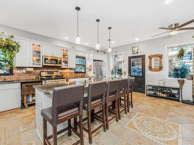 kitchen featuring a breakfast bar, hanging light fixtures, dark stone countertops, appliances with stainless steel finishes, and white cabinetry