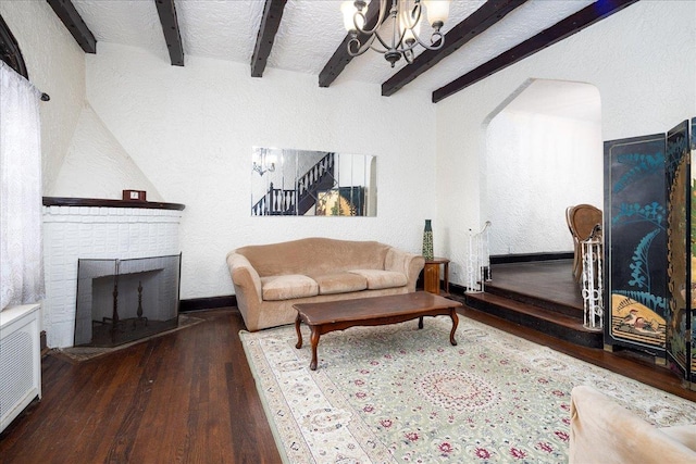 living room featuring a chandelier, beam ceiling, dark wood-type flooring, and a brick fireplace