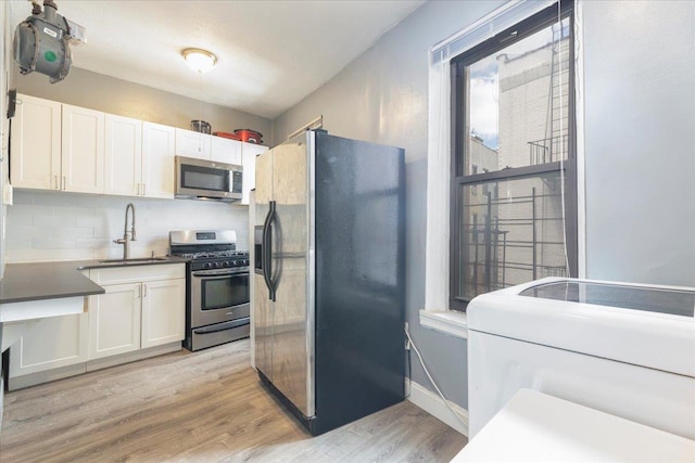 kitchen with sink, light hardwood / wood-style flooring, washer / dryer, white cabinets, and appliances with stainless steel finishes