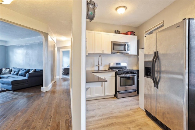 kitchen with backsplash, sink, light hardwood / wood-style flooring, appliances with stainless steel finishes, and white cabinetry