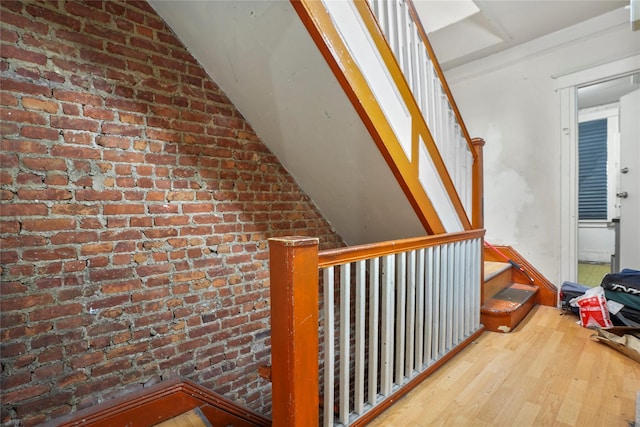 corridor with wood-type flooring, lofted ceiling, and brick wall