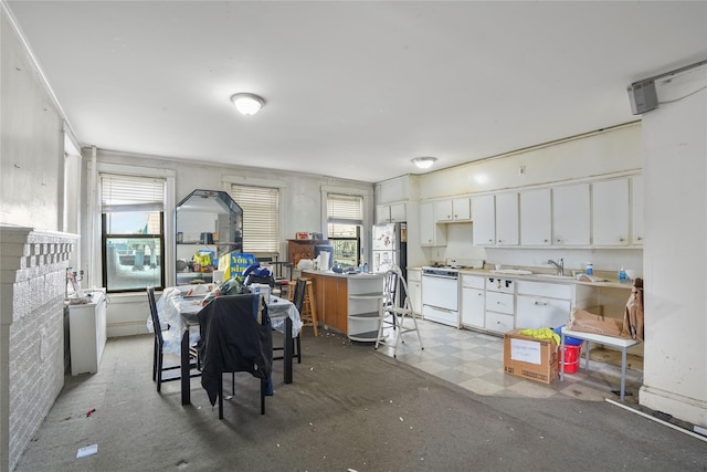 kitchen featuring stainless steel refrigerator, white cabinets, a healthy amount of sunlight, and white gas range oven