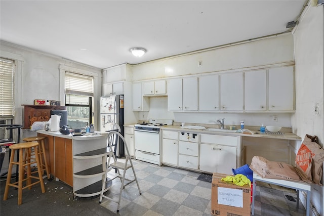 kitchen with white cabinets, sink, white range oven, kitchen peninsula, and stainless steel refrigerator