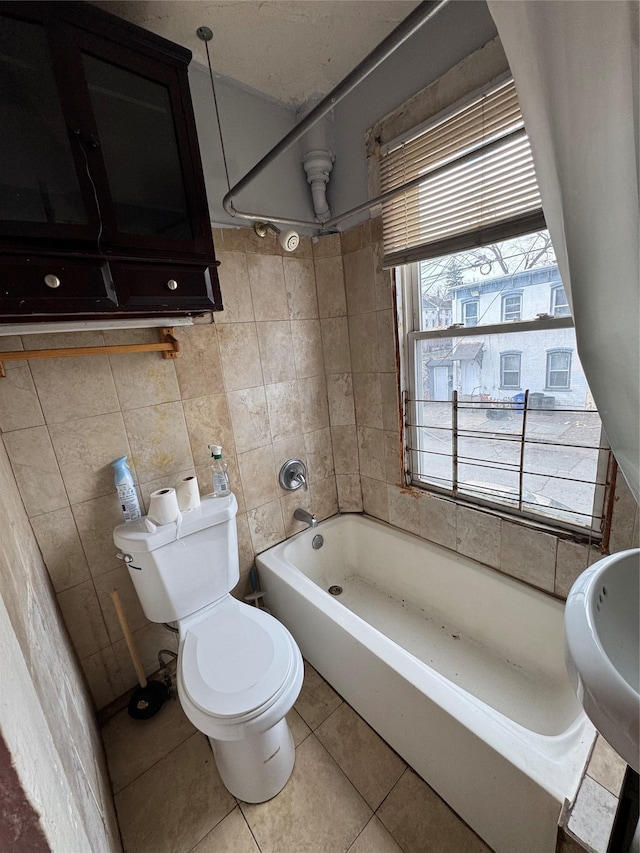 bathroom with tile patterned floors, washtub / shower combination, tile walls, and toilet