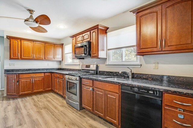 kitchen featuring ceiling fan, sink, dark stone countertops, black appliances, and light wood-type flooring