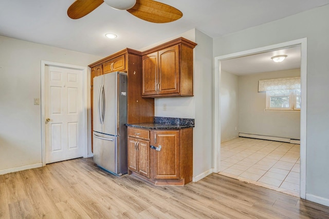 kitchen with stainless steel refrigerator, ceiling fan, a baseboard radiator, dark stone countertops, and light hardwood / wood-style floors