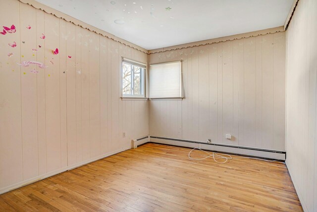 spare room with wood-type flooring, a baseboard heating unit, and wood walls