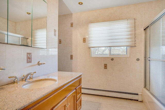 bathroom featuring baseboard heating, vanity, bath / shower combo with glass door, and tile walls