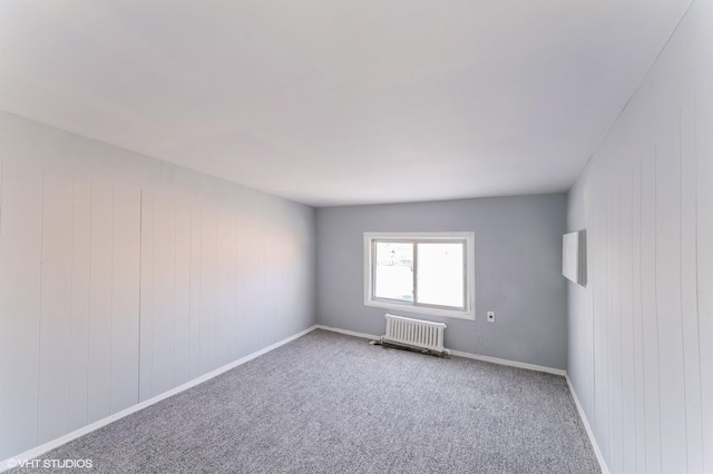 carpeted spare room with wooden walls and radiator heating unit