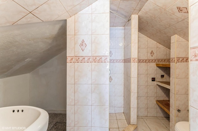 bathroom with tile patterned floors, a bath, tile walls, toilet, and lofted ceiling