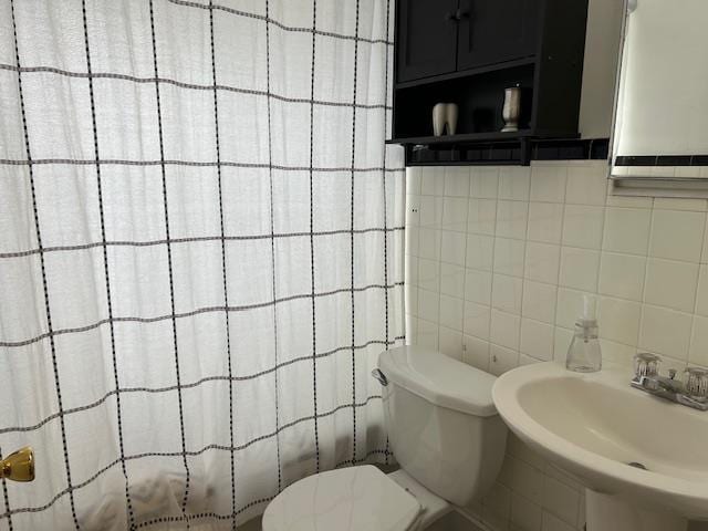 bathroom with backsplash, toilet, sink, and tile walls