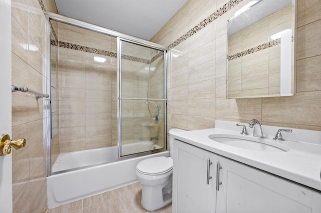 full bathroom featuring vanity, tile patterned floors, bath / shower combo with glass door, toilet, and tile walls