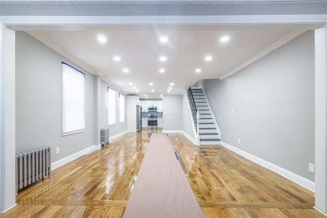 unfurnished living room with radiator, crown molding, and light wood-type flooring