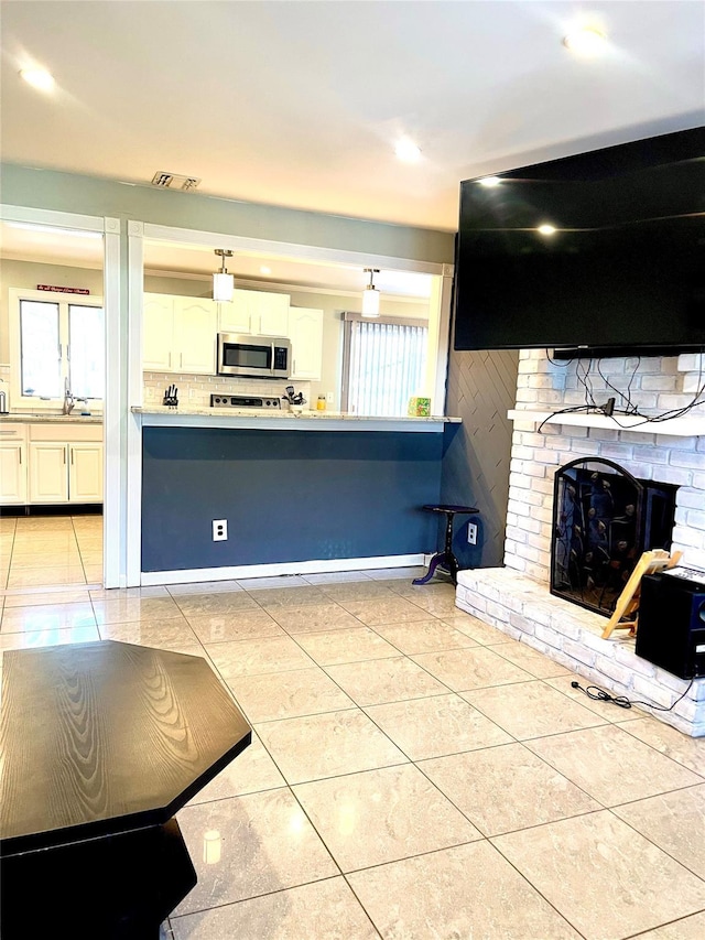 kitchen featuring decorative backsplash, a brick fireplace, sink, light tile patterned floors, and white cabinets