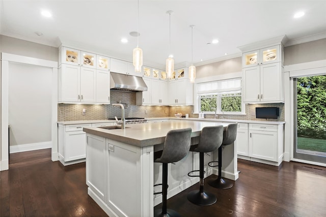 kitchen with an island with sink, pendant lighting, a kitchen bar, dark hardwood / wood-style floors, and white cabinetry