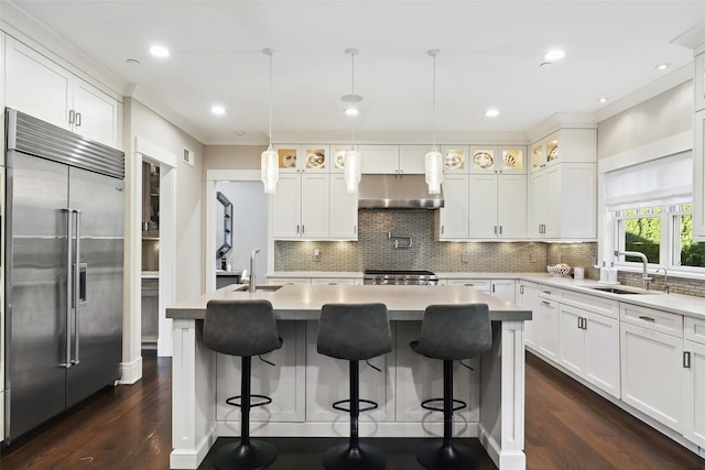 kitchen featuring pendant lighting, an island with sink, built in fridge, white cabinetry, and sink