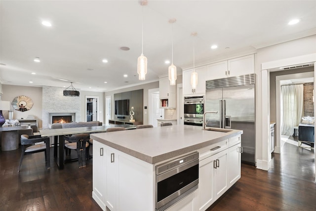 kitchen featuring built in appliances, a center island with sink, white cabinetry, and hanging light fixtures