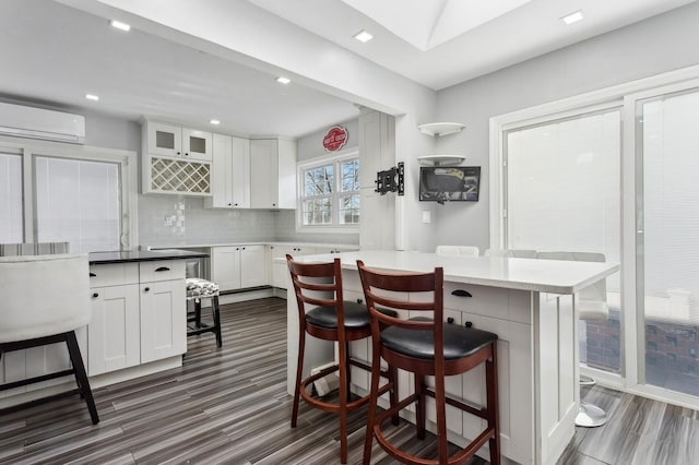 kitchen featuring white cabinetry, tasteful backsplash, dark hardwood / wood-style floors, an AC wall unit, and a breakfast bar