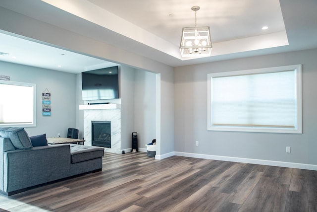 living room with a notable chandelier, dark hardwood / wood-style floors, a high end fireplace, and a tray ceiling