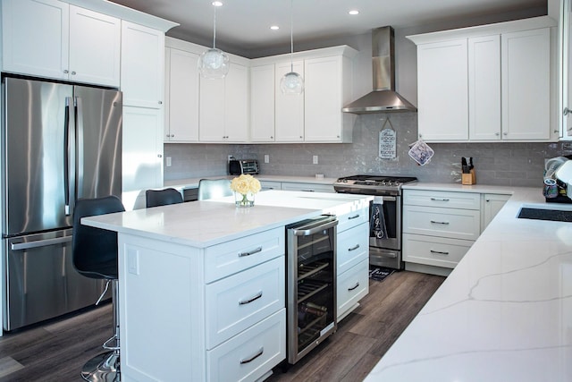 kitchen featuring pendant lighting, a breakfast bar, wall chimney range hood, appliances with stainless steel finishes, and beverage cooler