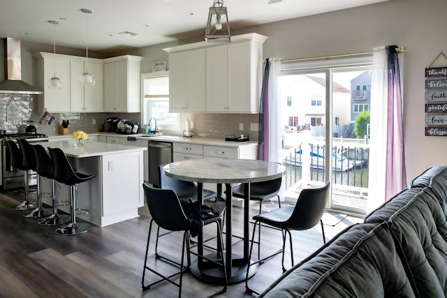 kitchen featuring pendant lighting, wall chimney exhaust hood, appliances with stainless steel finishes, a kitchen island, and white cabinetry