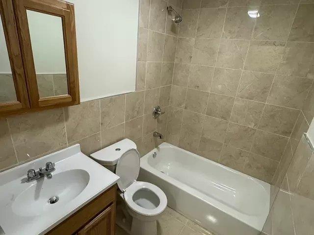 full bathroom with vanity, toilet, tile walls, and tiled shower / bath