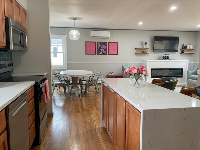 kitchen featuring a wall mounted AC, a kitchen island, decorative light fixtures, and appliances with stainless steel finishes