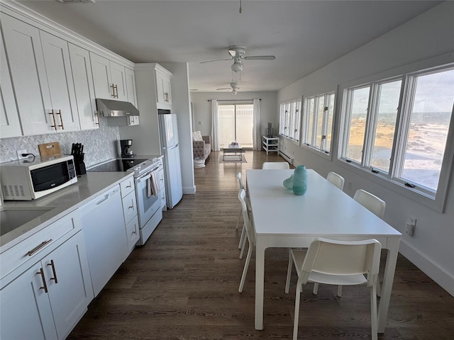 kitchen with white cabinetry, a kitchen bar, dark hardwood / wood-style floors, backsplash, and white appliances