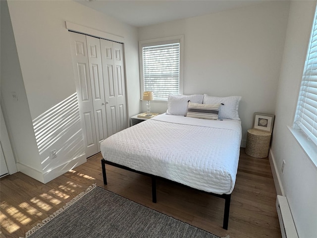 bedroom with dark wood-type flooring, a baseboard radiator, and a closet