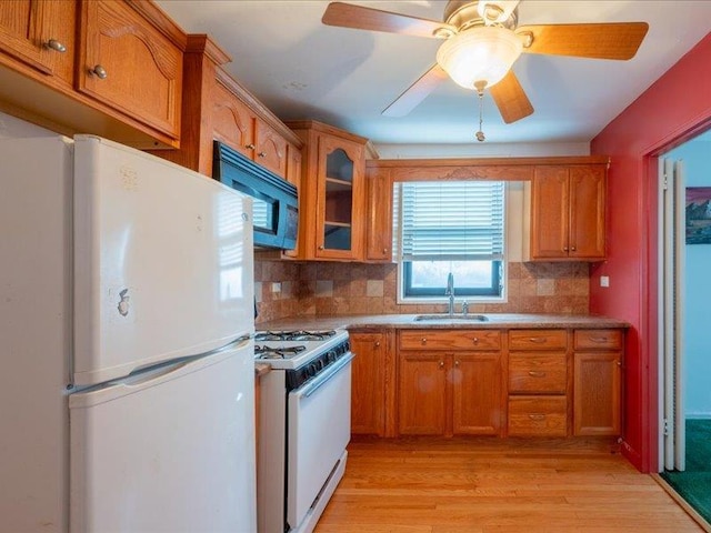 kitchen with decorative backsplash, white appliances, light hardwood / wood-style floors, and sink