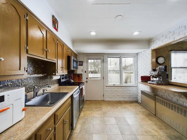 kitchen with sink, a wealth of natural light, radiator heating unit, stainless steel appliances, and brick wall