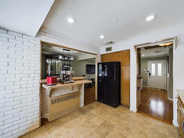 kitchen featuring pendant lighting, black fridge, light tile patterned floors, and brick wall