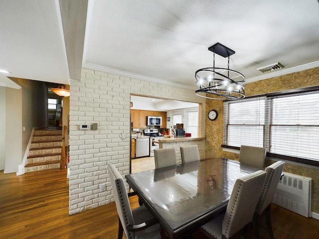 dining area featuring light wood-type flooring, an inviting chandelier, ornamental molding, and brick wall