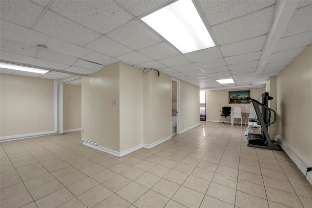 basement featuring a drop ceiling, light tile patterned flooring, and baseboard heating