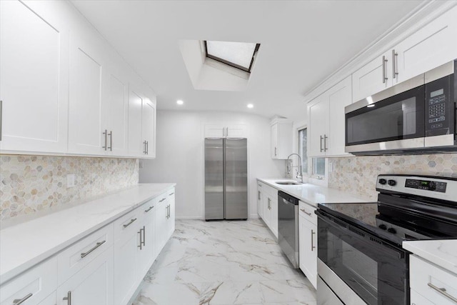 kitchen with a skylight, sink, stainless steel appliances, decorative backsplash, and white cabinets