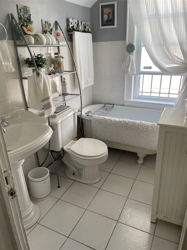 bathroom with a bathtub, sink, tile patterned flooring, toilet, and tile walls