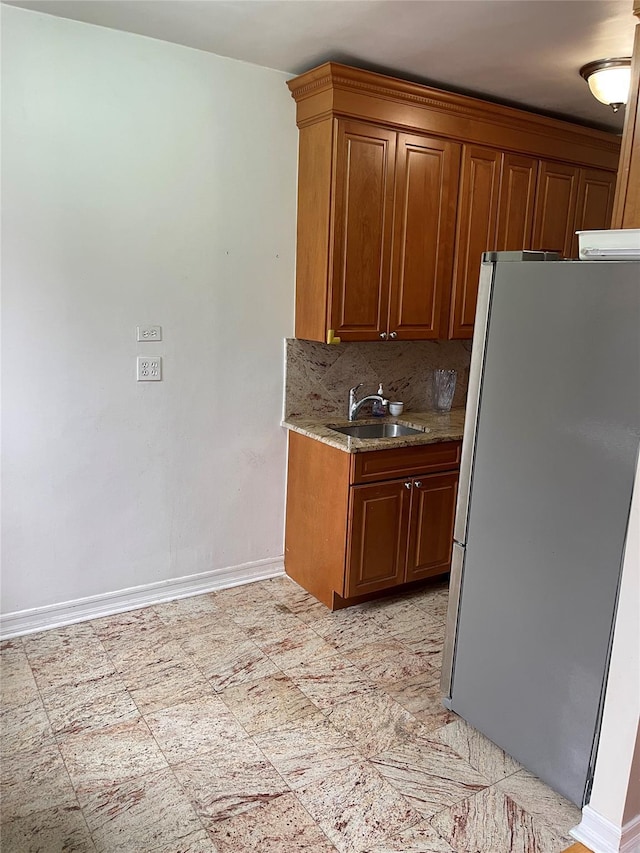 kitchen featuring light stone countertops, refrigerator, backsplash, and sink