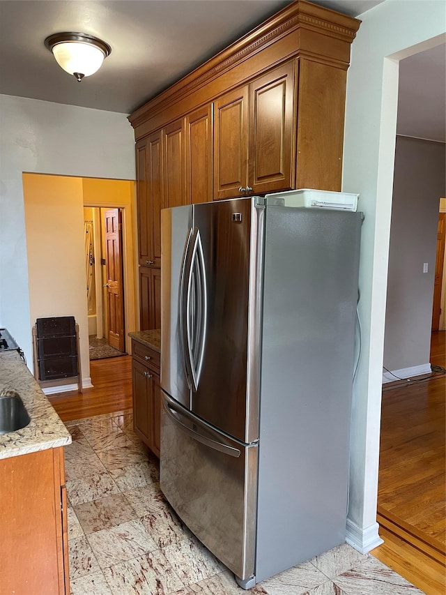 kitchen with stainless steel fridge, light wood-type flooring, and light stone counters