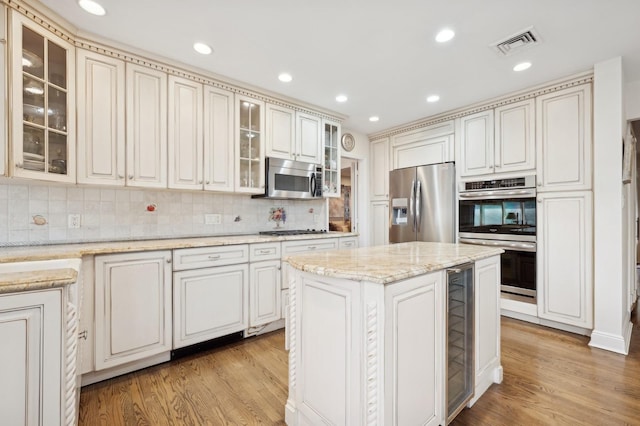 kitchen featuring light hardwood / wood-style flooring, appliances with stainless steel finishes, tasteful backsplash, a kitchen island, and light stone counters