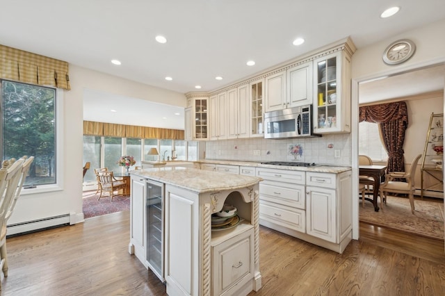 kitchen featuring light stone countertops, appliances with stainless steel finishes, baseboard heating, light hardwood / wood-style flooring, and a center island