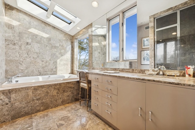 bathroom with a skylight, vanity, a relaxing tiled tub, and tile walls