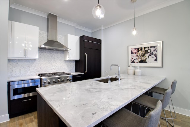 kitchen featuring pendant lighting, high quality appliances, white cabinets, wall chimney exhaust hood, and a kitchen bar