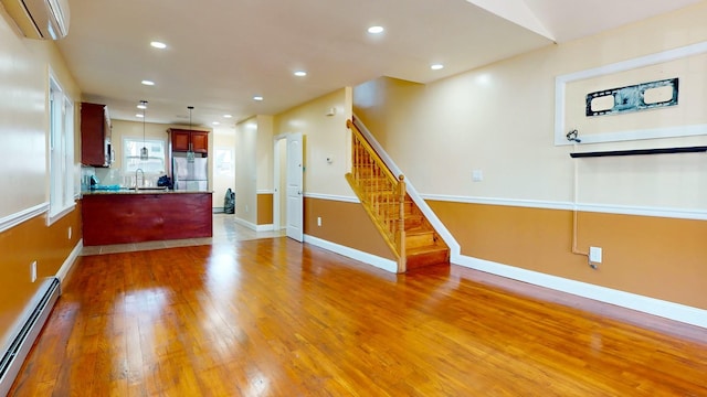 unfurnished living room with a wall mounted air conditioner, dark wood-type flooring, a baseboard heating unit, and sink