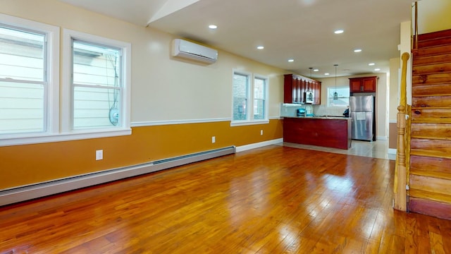 kitchen with stainless steel refrigerator, a baseboard heating unit, a wall unit AC, light hardwood / wood-style floors, and pendant lighting