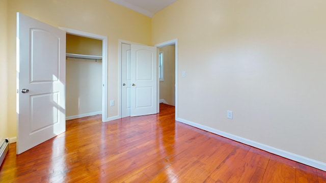 unfurnished bedroom with hardwood / wood-style floors and baseboard heating