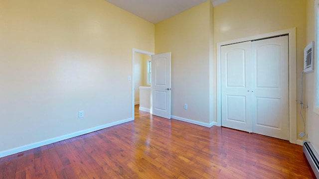 unfurnished bedroom featuring dark hardwood / wood-style floors, a closet, and a baseboard heating unit