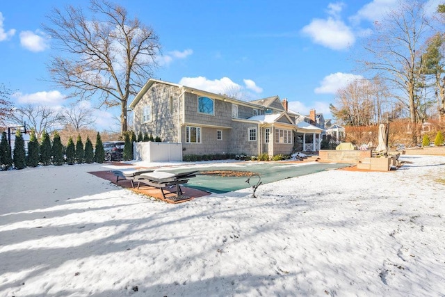 snow covered back of property with a covered pool